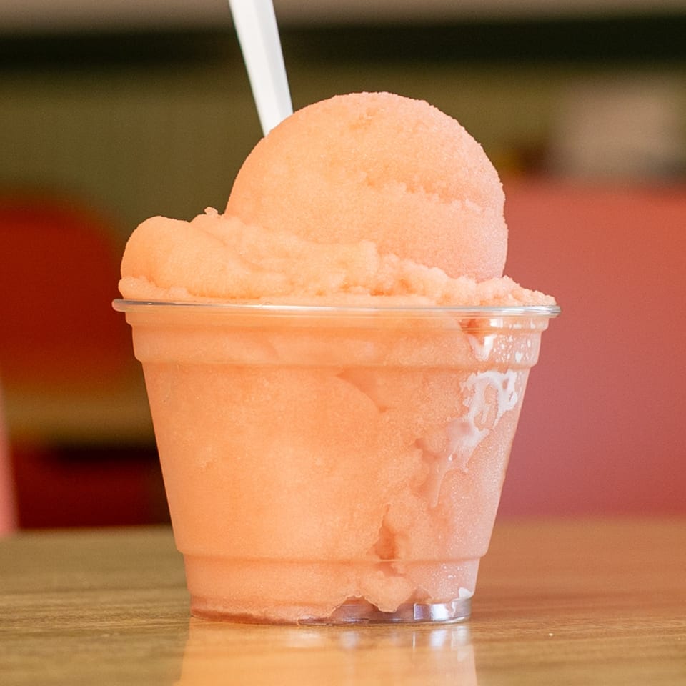 A clear plastic cup filled with a light orange sorbet, topped with a white spoon.