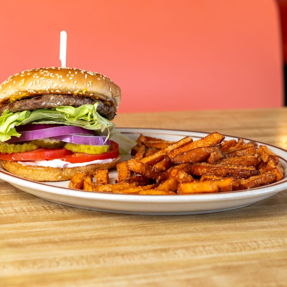 A hamburger with lettuce, onion, pickles, and tomato, served with a side of sweet potato fries.