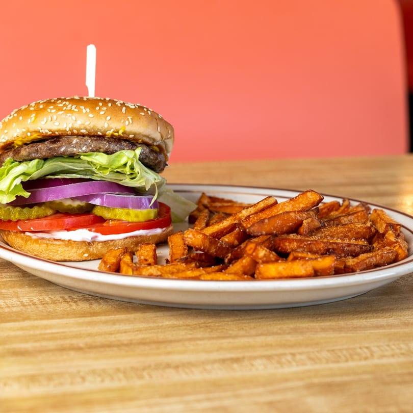 A hamburger with lettuce, onion, pickles, and tomato, served with a side of sweet potato fries.
