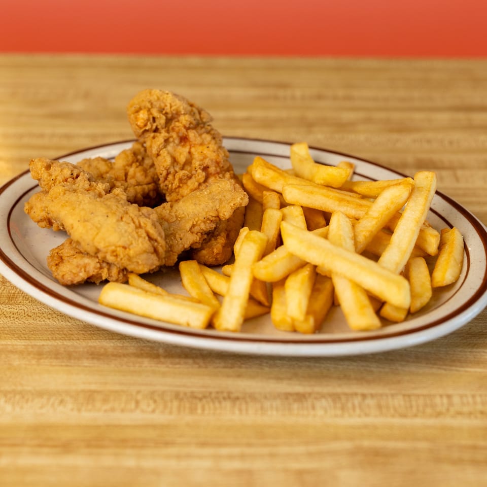 A plate of crispy fried chicken tenders and golden french fries on a wooden table.