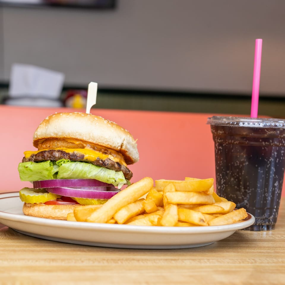 Cheeseburger with onion rings, lettuce, tomato, and pickles, served with fries and a soda.