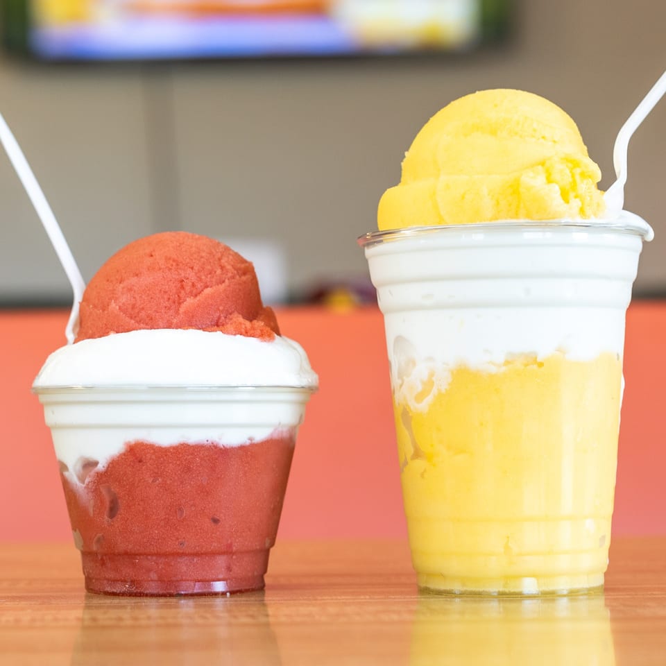 Two colorful fruit smoothies, one red and one yellow, with scoops of sorbet on top.