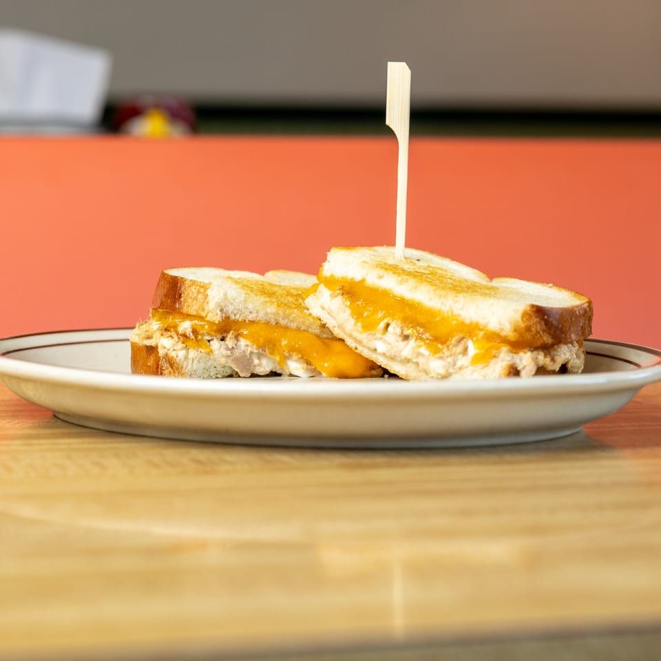 Two halves of a grilled cheese sandwich with tuna salad, served on a white plate.